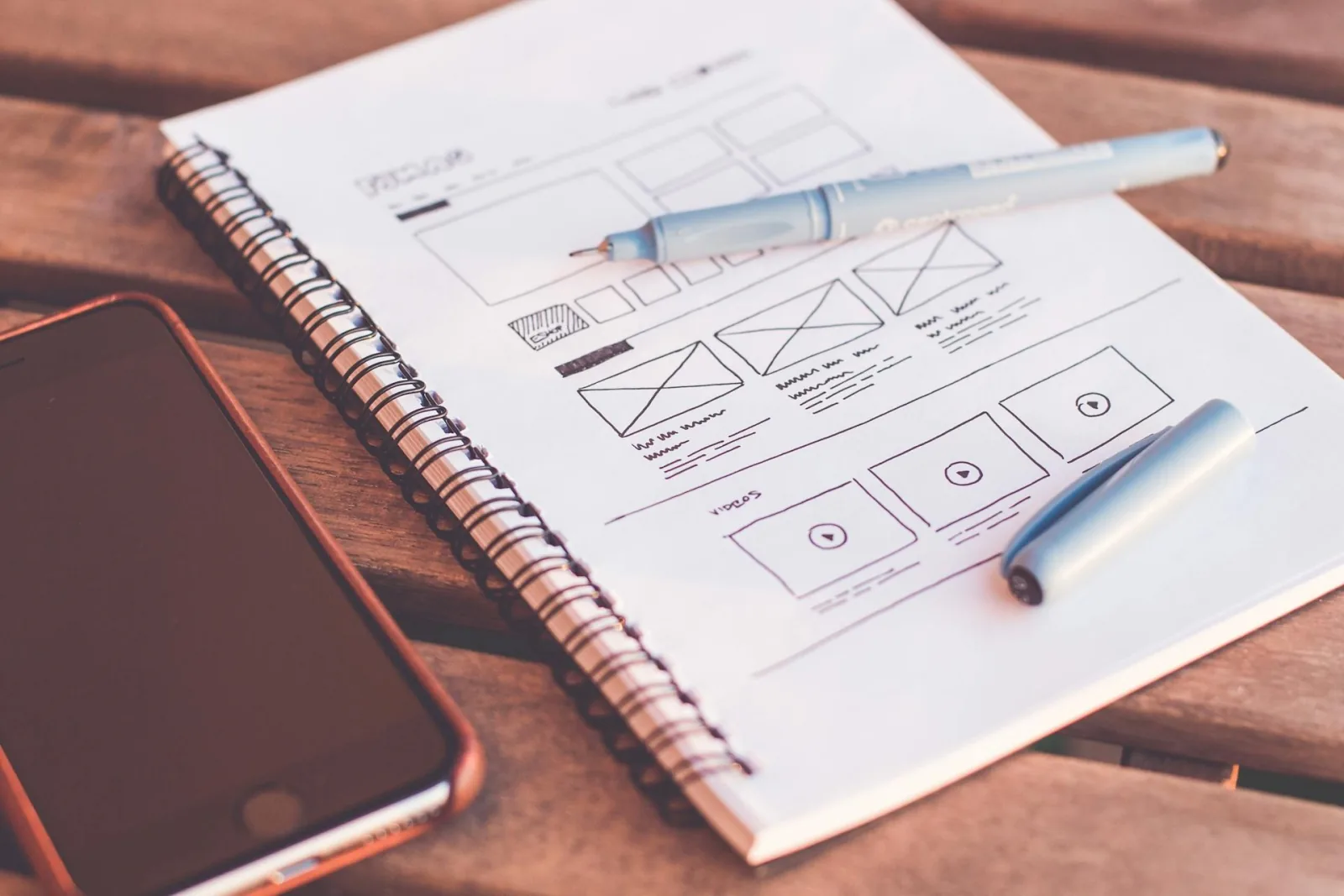 Hand-drawn website wireframe in notebook beside phone, planning sales page copy